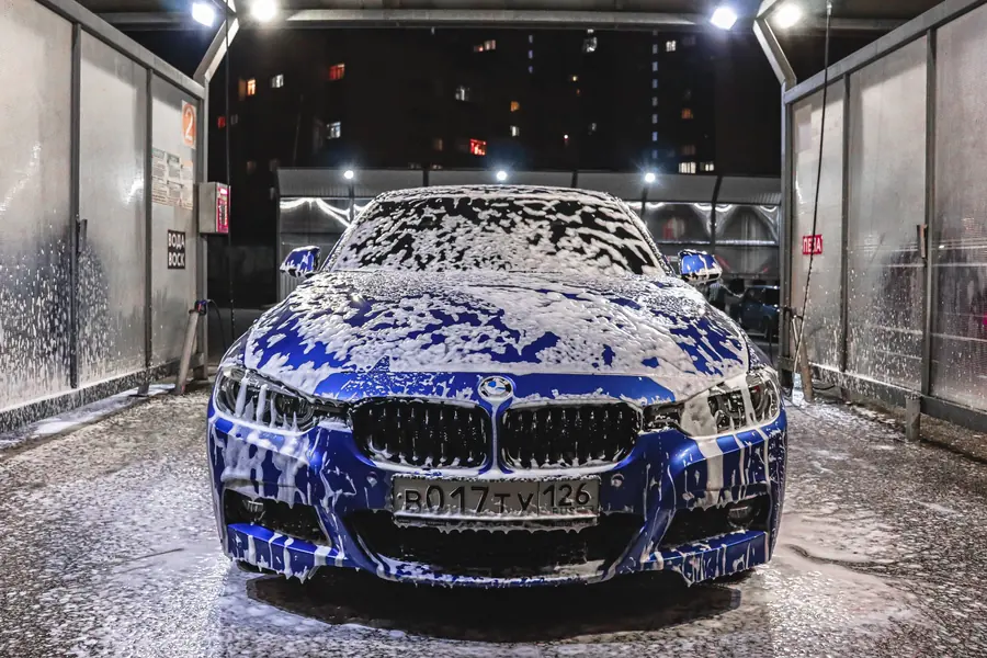 Autolavado premium: BMW cubierto de espuma azul en cabina de lavado de lujo