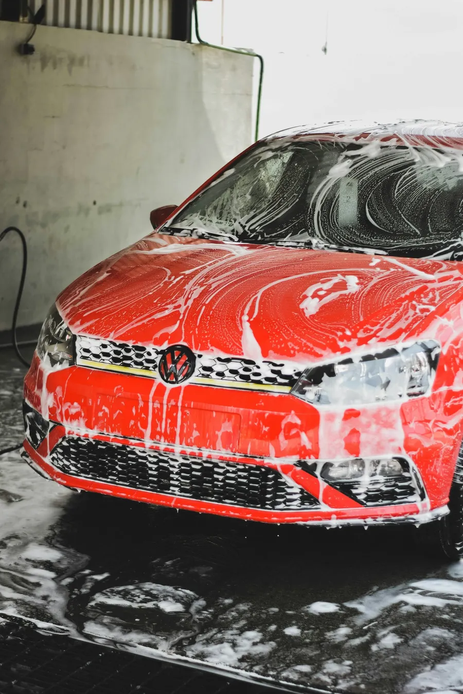 Auto lavado express: Auto rojo cubierto de espuma activa durante el lavado