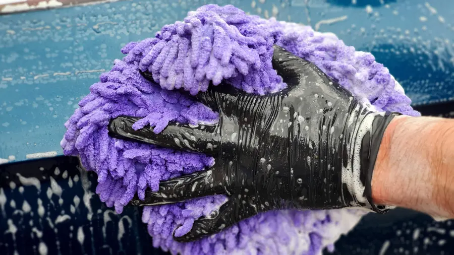 Autolavado cerca de mi: Guante de microfibra morado sobre pintura negra con espuma