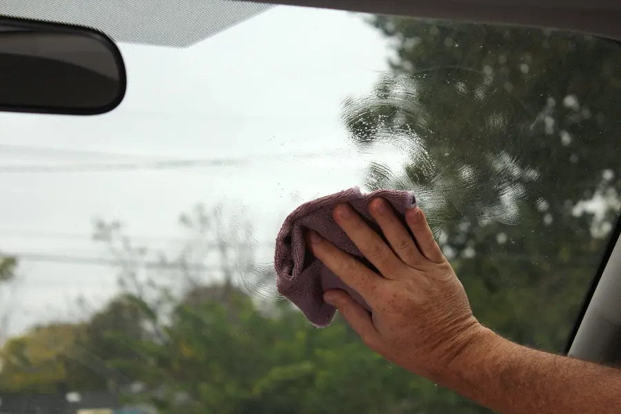 Lavado en seco autos: Mano limpiando el parabrisas con paño de microfibra